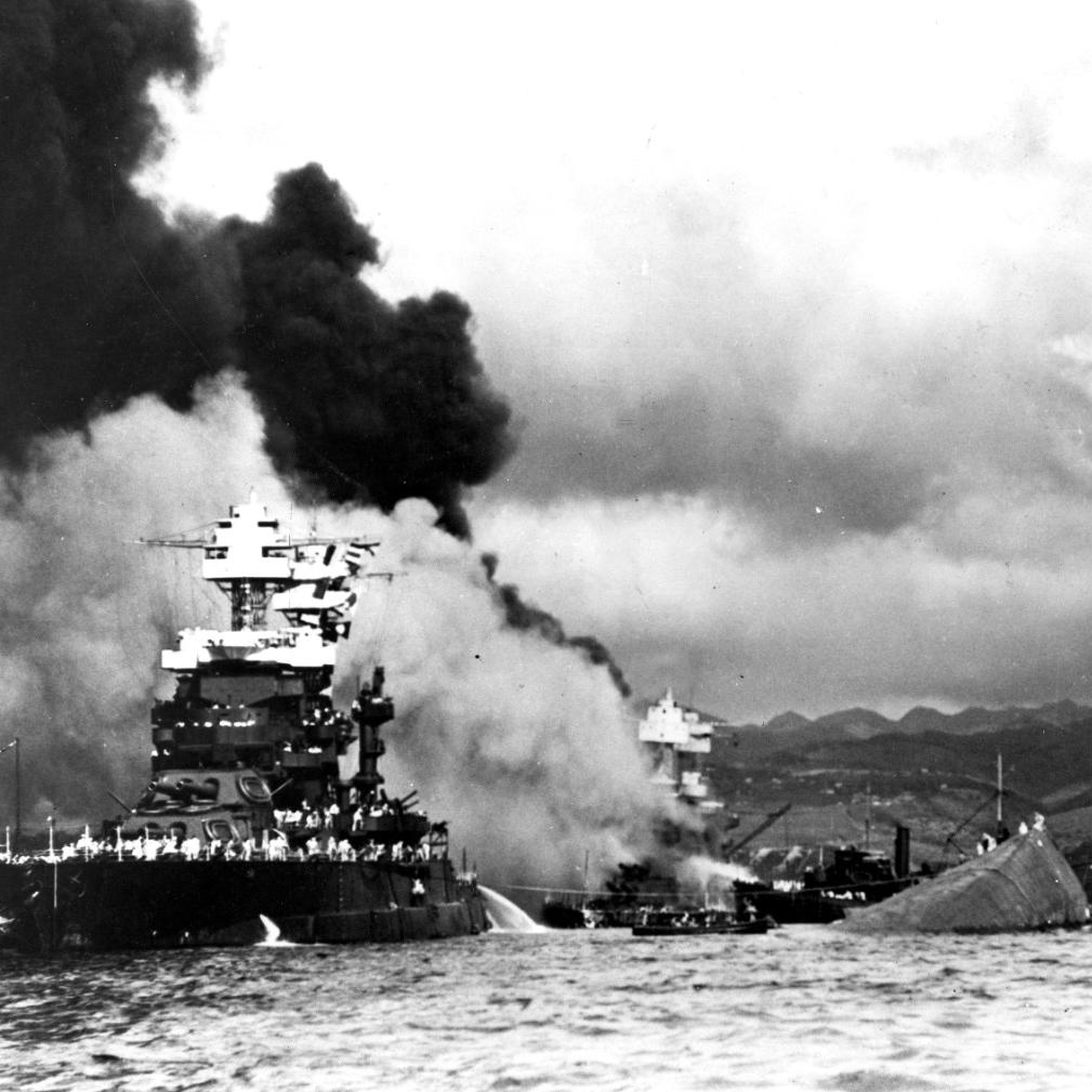 USS Maryland (BB-46) alongside the capsized USS Oklahoma (BB-37). USS West Virginia (BB-48) is burning in the background.