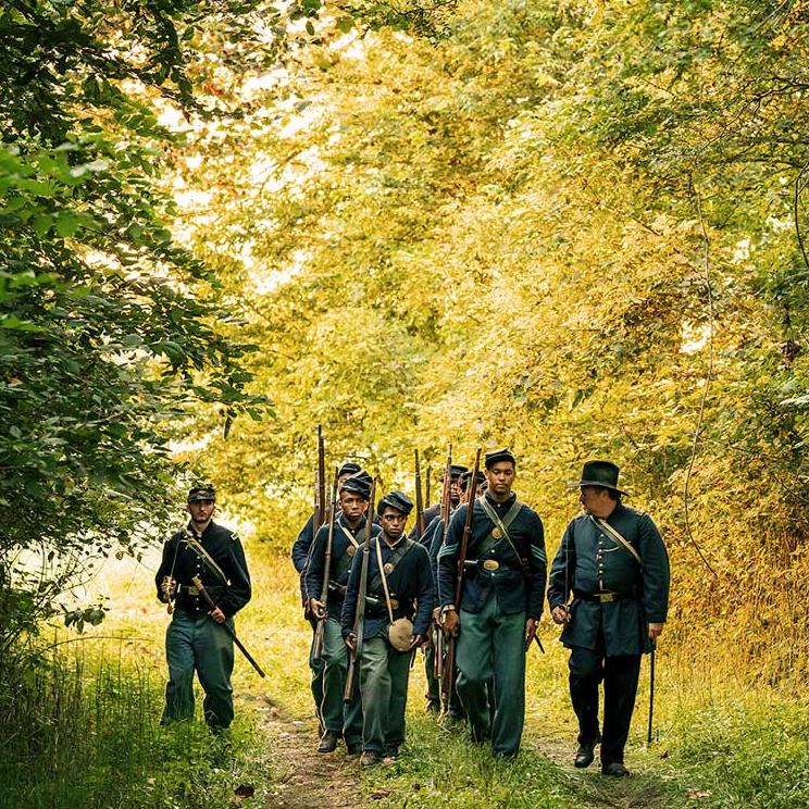 A photograph of USCT reenactors marching through the woods